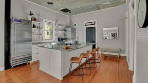 A modern kitchen with a large island, bar stools, and a refrigerator. - Gorgeous Home 1 Blk From Main With Hot Tub & Fire Pit! (Fredericksburg)