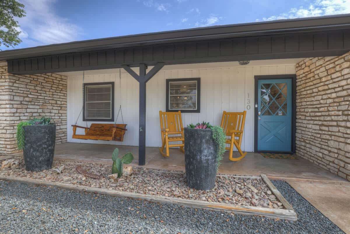 A building with a stone facade, a blue door, and a porch with two chairs and a swing.