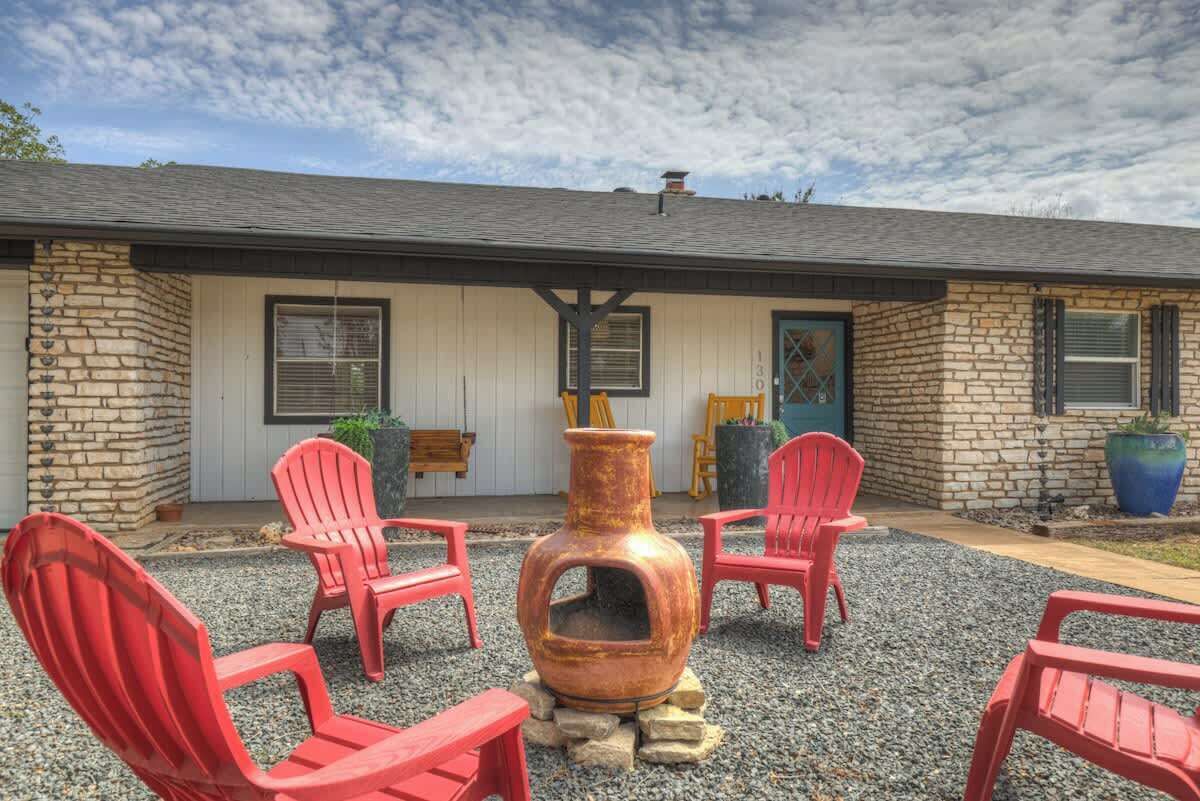 A building with a stone facade, a front door, and a large window. There are four red Adirondack chairs arranged in front of the building.