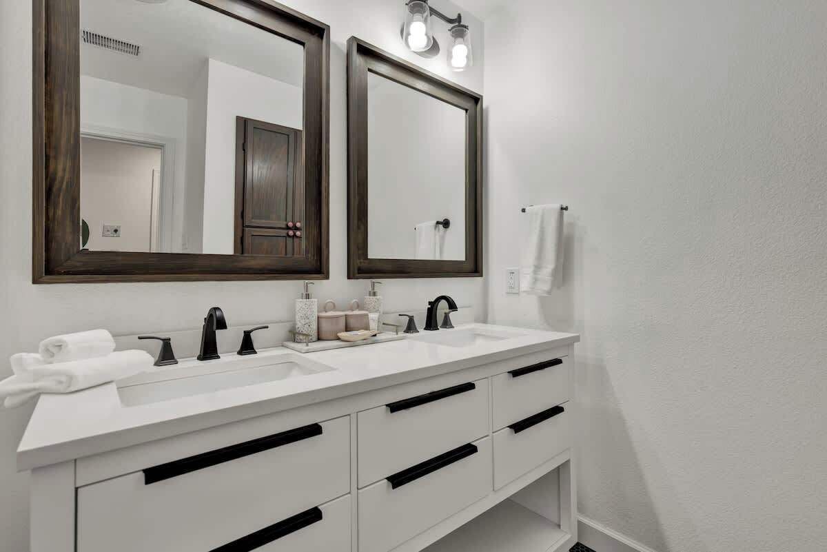 A modern bathroom with two sinks, dark wooden mirrors, and white cabinetry.