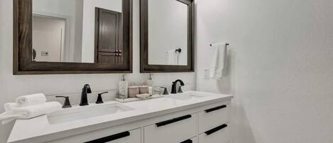 Un baño moderno con dos lavamanos, espejos de madera oscura y muebles de color blanco.