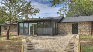A modern building with a stone exterior and a glass-enclosed patio area. - Eclectic Fun Haus With Hot Tub - 3 Min Drive to Main (Fredericksburg)