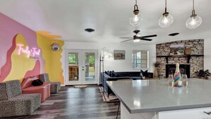 A modern living room with a large island, a fireplace, and a neon sign on the wall. - Eclectic Fun Haus With Hot Tub - 3 Min Drive to Main (Fredericksburg)