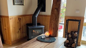 Une table à manger en bois avec des bancs, un poêle en bois noir, une bougie et un tableau encadré au mur.