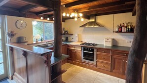 Une cuisine avec des meubles en bois, un four encastré, un évier et une fenêtre donnant sur un paysage verdoyant.
