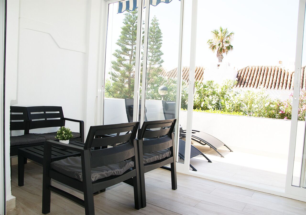 A modern room with two black chairs and a small table, large windows with a view of greenery and a building outside.