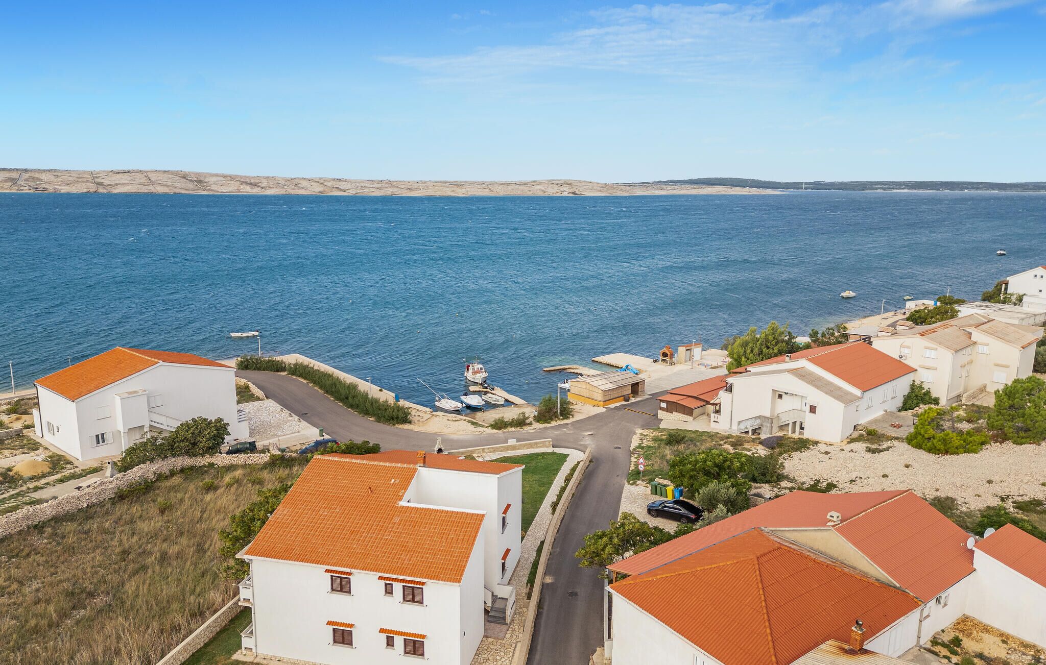 A coastal residential area with white buildings, red-tiled roofs, and a clear view of the sea.