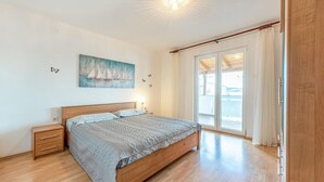 Ein Schlafzimmer mit einem hölzernen Bett, einem Nachttisch, einem Segelbootbild und einem großen Fenster mit Vorhängen.