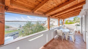 Ein überdachter Balkon mit Meerblick, inklusive Tisch und Stühlen sowie einer Steinmauer.