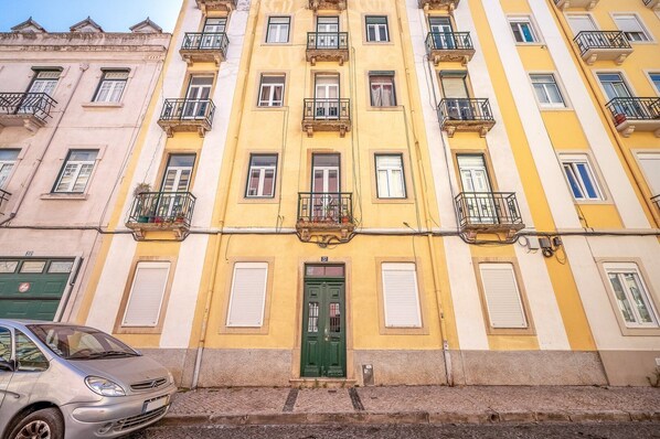 A multi-story building with balconies, a green door, and a parked car.