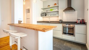 Ett modernt kök med vita skåp, en bardisk i trä och två barstolar.