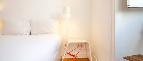 A bedroom with a bed, a standing heater, and a wooden floor.