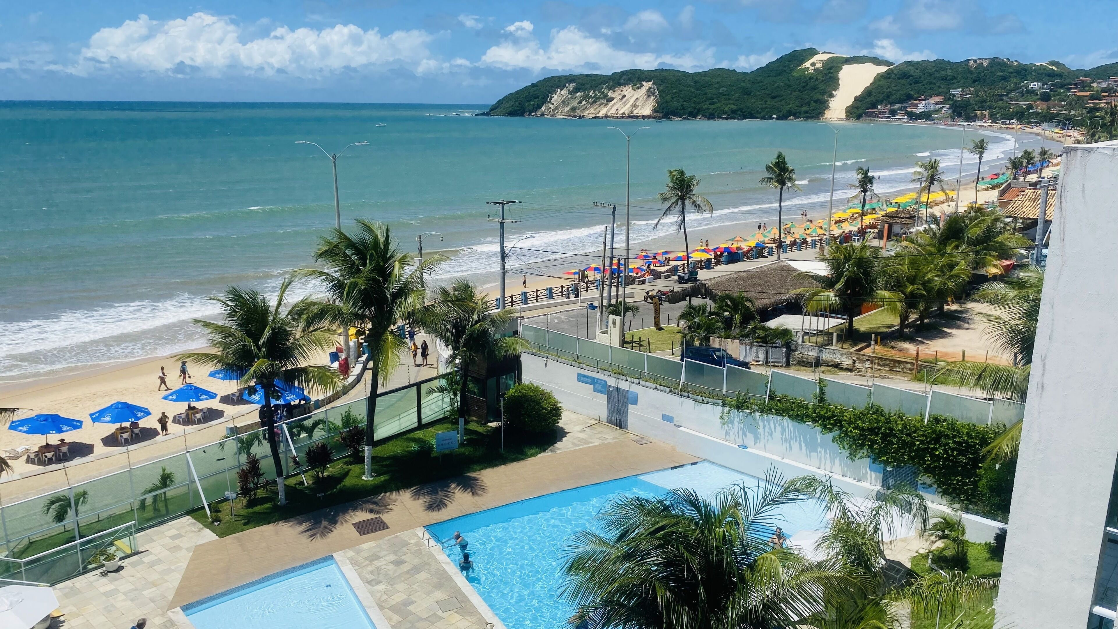 Um resort à beira-mar com piscina, guarda-sóis e vista para o oceano.