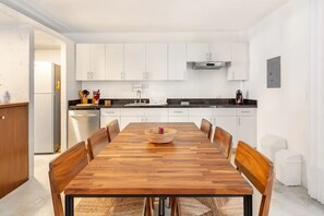 A modern kitchen with white cabinets, a wooden dining table, and a built-in oven. - Design Apartment, 2 Bedroom, Deck and Garden View (Tulum)