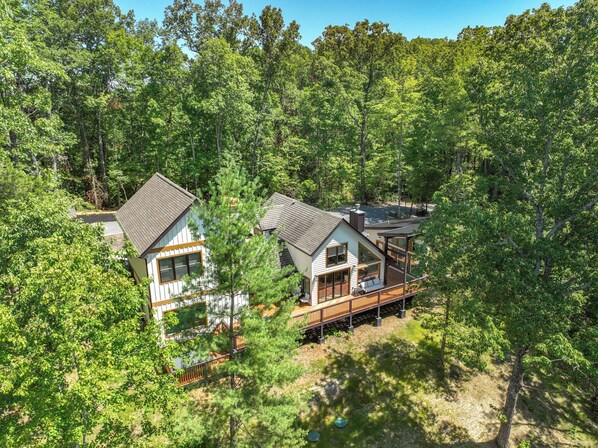 A modern cabin with a deck and large windows, surrounded by dense forest.