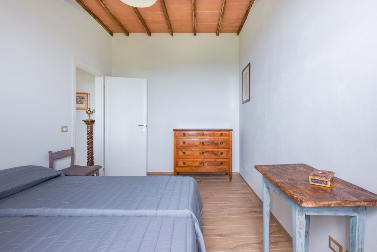 Un dormitori amb llit, un taulell de fusta, una taula petita i una porta que dona a una altra habitació.