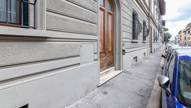 A building with a large wooden door, a window with a metal grille, and a parked car on the street. - GuestHost - Elegant apartment of 80 sqm, able to accommodate up to 5 people, located on the 2nd floor of a building equipped with a lift (NOT suitable for disabled people - some steps to access). The property is located in the Stibbert/Statuto area, a li (Firenze)