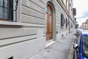 A building with a large wooden door, a window with a metal grille, and a parked car on the street.