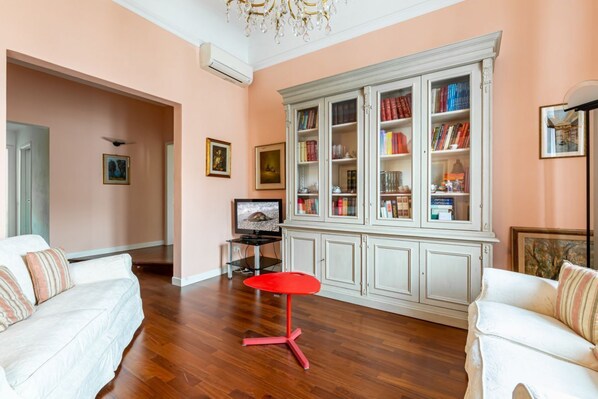 A living room with a white sofa, a red stool, a white cabinet with books, and a television.