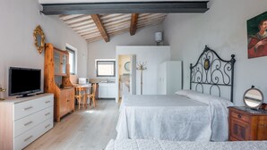 Ein Schlafzimmer mit Bett, Fernseher, einem Holzschrank, einem Schreibtisch und einer Küchenzeile.