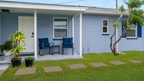 A house with a porch, two blue chairs, and potted plants.