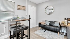 A modern living room with a black leather sofa, a wooden coffee table, and a round mirror on the wall.