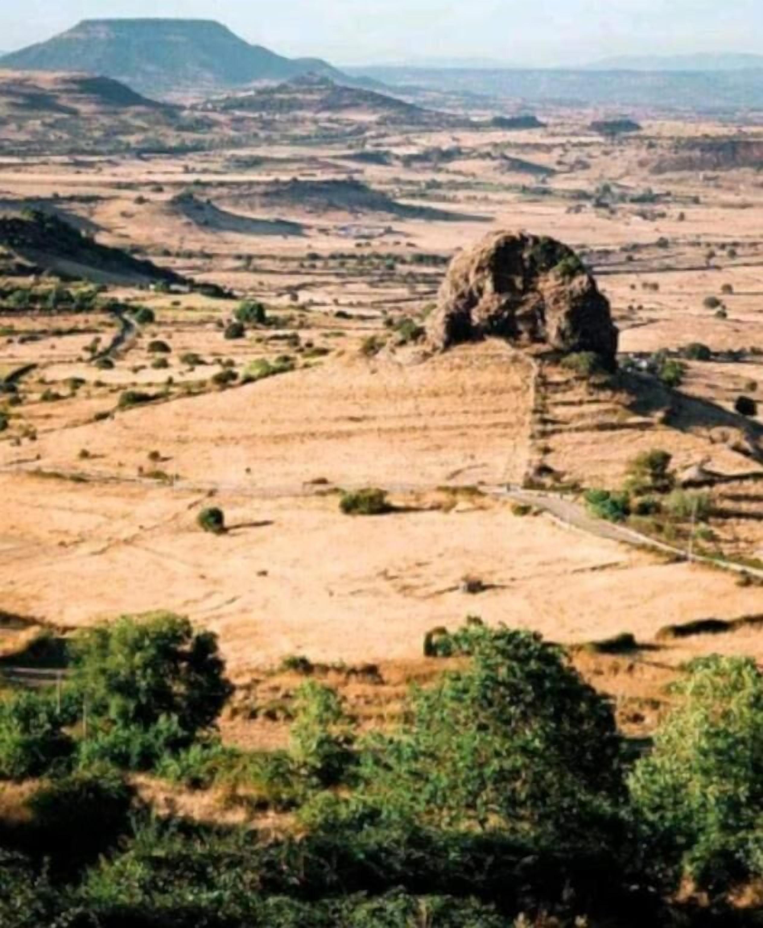 Eine weite, offene Landschaft mit terrassierten Feldern und einer markanten Felsformation.