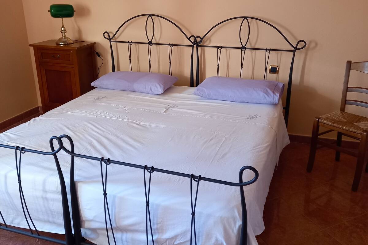 A neatly made bed with a metal frame, a wooden nightstand with a lamp, and a chair.