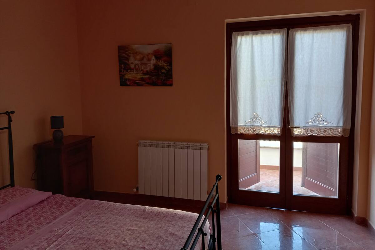 A bedroom with a bed, a radiator, a painting, and a window with curtains.
