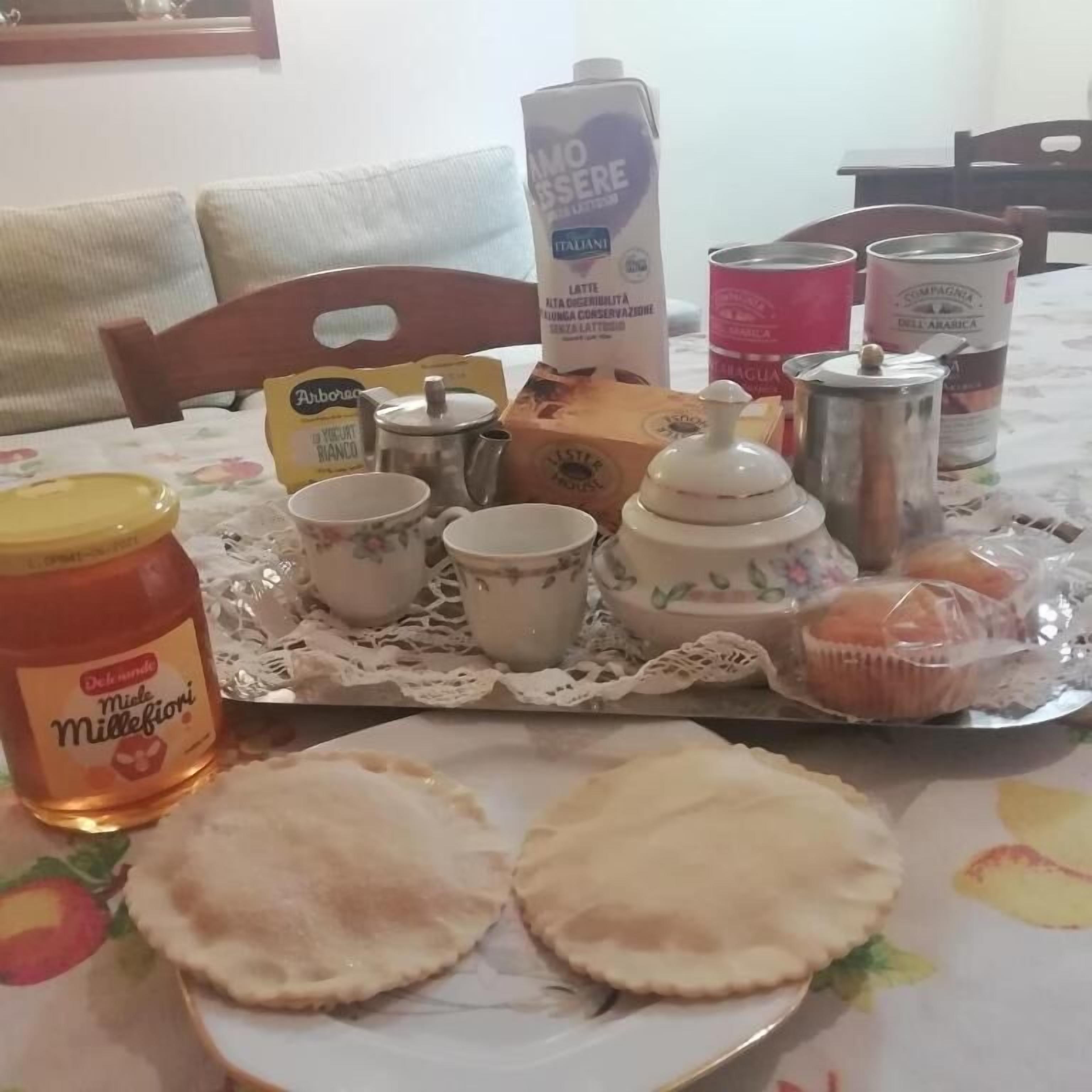 Ein Esstisch ist gedeckt mit verschiedenen Gegenständen, darunter ein Glas Miele Millefiori Honig, eine Milchpackung, eine Biscotti-Schachtel und mehrere Tassen mit Untertassen.