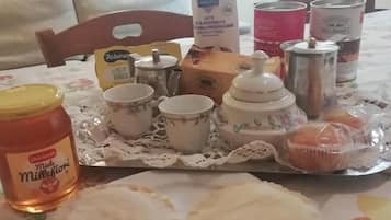 Ein Esstisch ist gedeckt mit verschiedenen Gegenständen, darunter ein Glas Miele Millefiori Honig, eine Milchpackung, eine Biscotti-Schachtel und mehrere Tassen mit Untertassen.