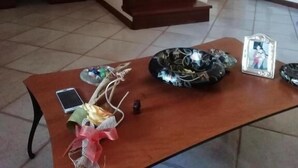 Uma sala de estar ampla com escada de madeira, uma mesa de jantar com um vaso e molduras de quadros, e uma pintura na parede.