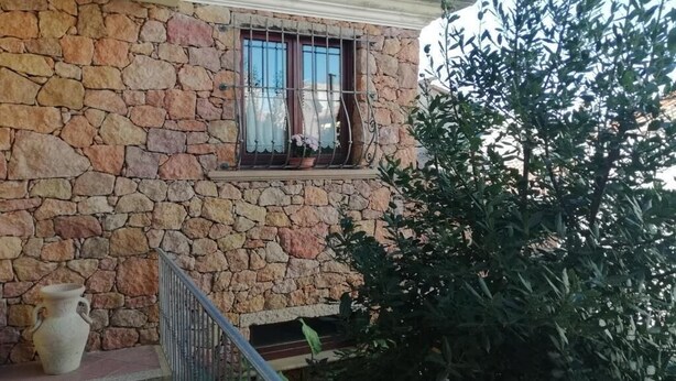 Um edifício de pedra com uma janela, um pequeno alpendre e um vaso de planta.