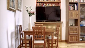 Een woonkamer met een houten eettafel, vier stoelen, een flatscreen televisie, een boekenkast en een kast met glazen deuren.
