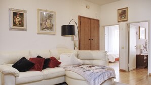 Een woonkamer met een witte leren bank, een houten deur en een lamp.