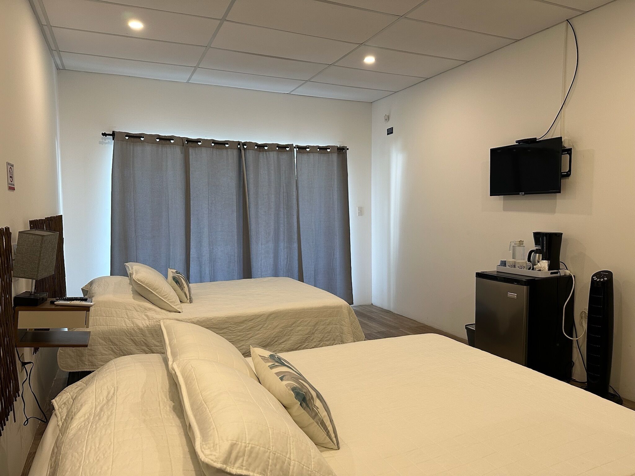 Een hotelkamer met twee bedden, een bureau met lamp, een televisie, een koffiezetapparaat en een koelkast.