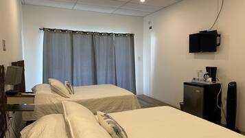 Een hotelkamer met twee bedden, een bureau met lamp, een televisie, een koffiezetapparaat en een koelkast.