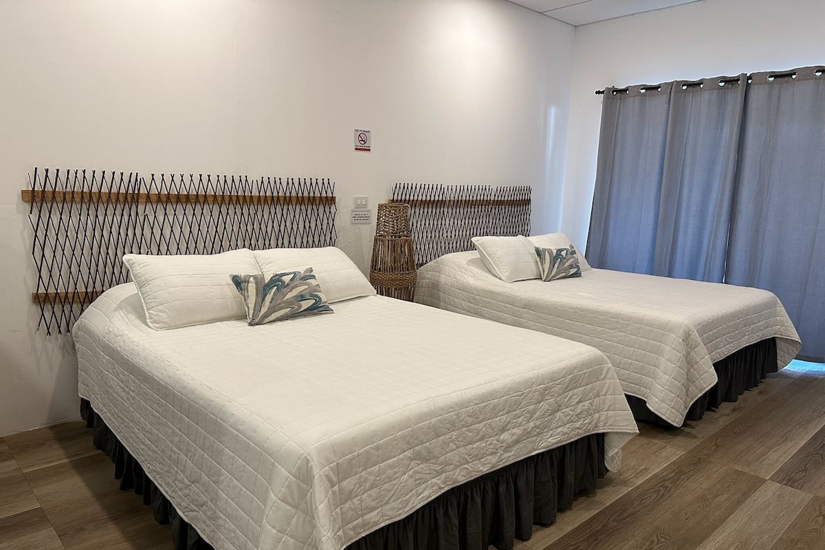 Two single beds with white bedding and dark skirts, a wooden floor, and a window with curtains.