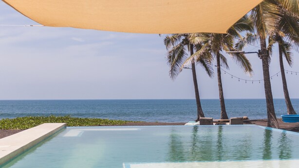 Una piscina amb vistes a l'oceà, palmeres i una zona d'ombra.