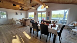 Un vaste espace de vie doté d’un plafond en bois, d’une table à manger pour quatre personnes et d’une grande fenêtre donnant sur un lac.