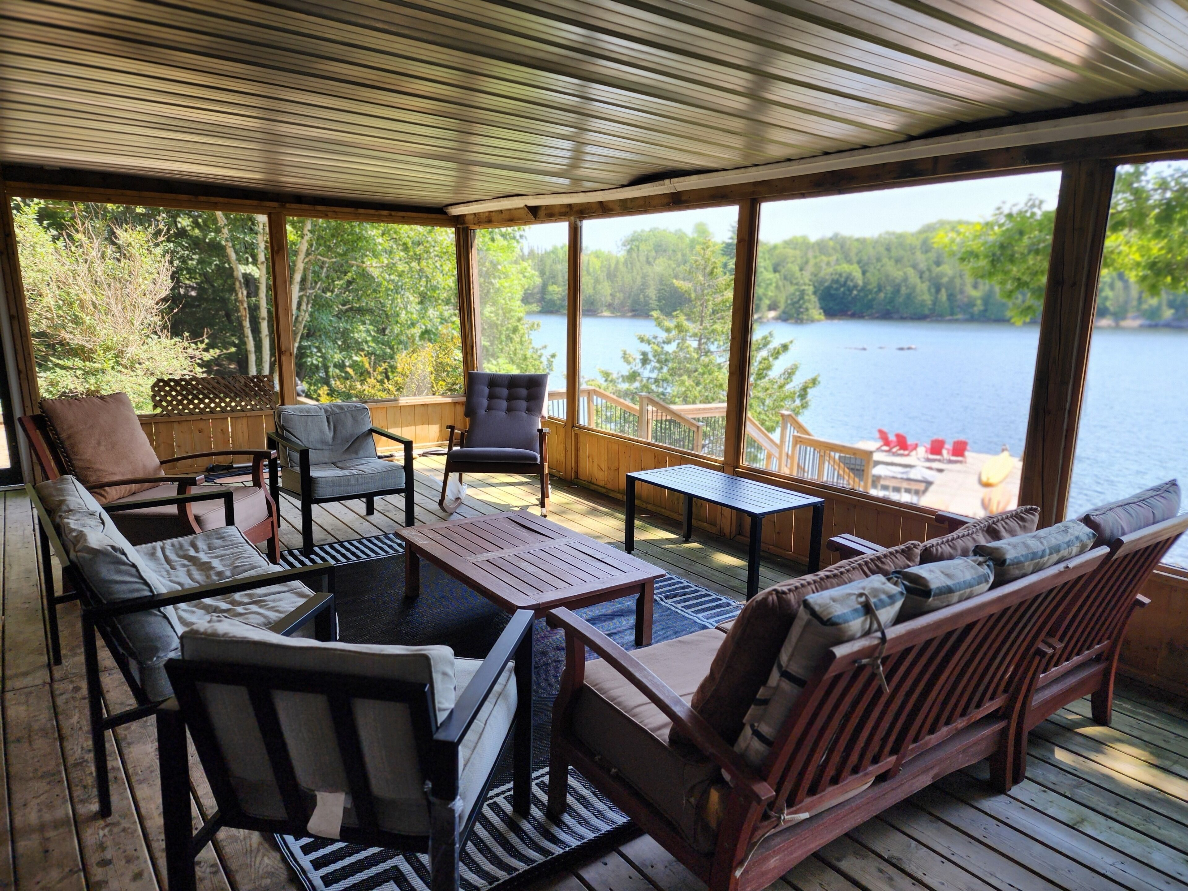 Un espace extérieur abrité, aménagé avec du mobilier en bois et offrant une vue sur un lac.