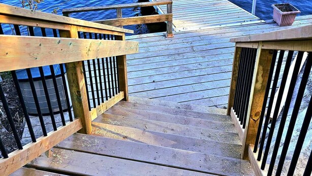 Un escalier en bois mène à une jetée où se trouvent une barque à rames et des chaises rouges.