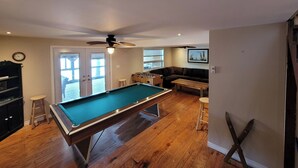 Une table de billard dans une pièce équipée d’un ventilateur de plafond, d’un canapé et d’une table de baby-foot.