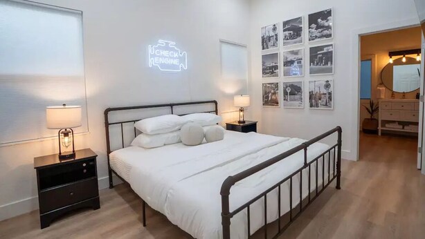 A bedroom with a bed, bedside tables, a wall-mounted neon sign, and framed pictures. - Kerrville Texaco
 (Kerrville)