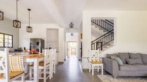 Amplia sala de estar con una mesa de comedor, sillas blancas, un sofá gris y una escalera.