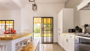 Una cocina moderna con armarios blancos, una banca de madera, una mesa de comedor y vistas al exterior a través de un ventanal.