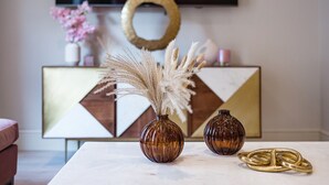 Two brown glass vases with pampas grass on a white table, a gold ring, and a geometric-patterned cabinet with a television above. - Marble Arch Suite 3-Hosted by Sweetstay (London)