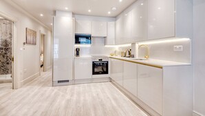 A modern kitchen with white cabinetry, a built-in oven, a microwave, and a gold-colored faucet. - Marble Arch Suite 3-Hosted by Sweetstay (London)
