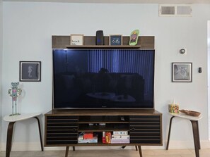 Een woonkamer met een grote flatscreen televisie, een houten entertainmentkast en ingelijste foto’s aan de wand.
