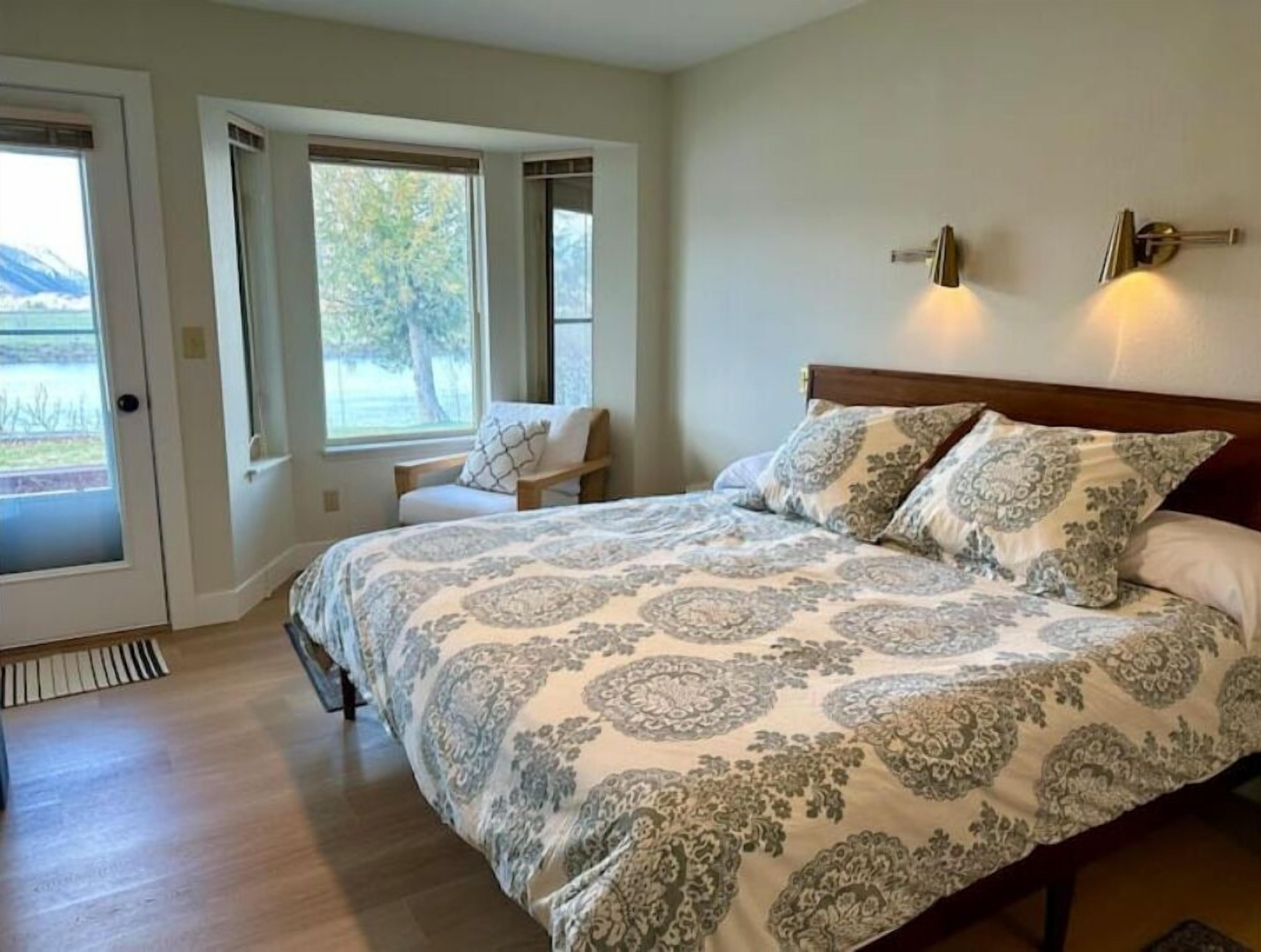 A bedroom with a large bed, two windows, a chair, and a door.